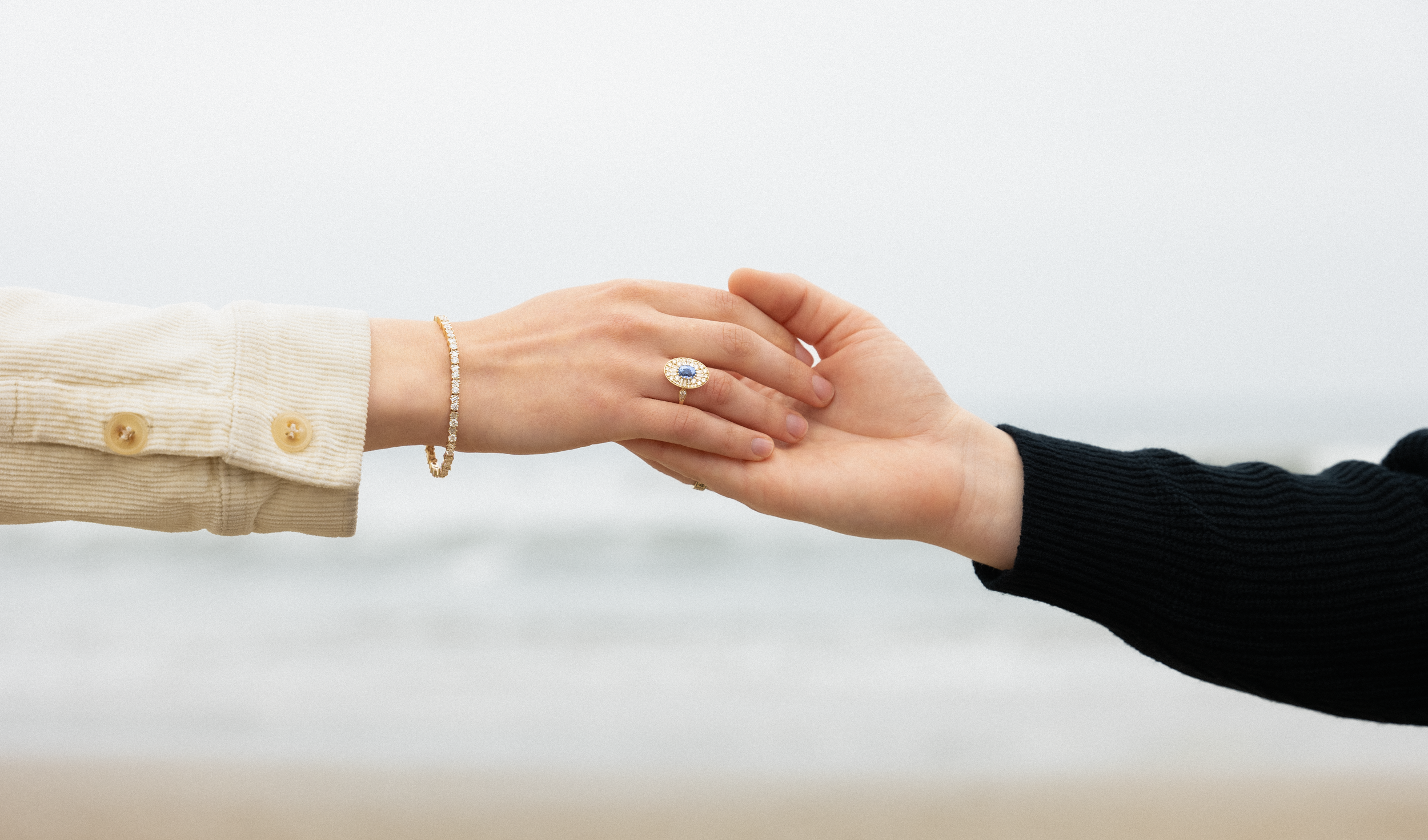 Couple holding hand and woman wearing yellow gold diamond tennis bracelet and sapphire diamond engagement ring
