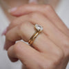 Woman wearing a pear shaped opalescent diamond ring paired with criss cross engraved wedding band.