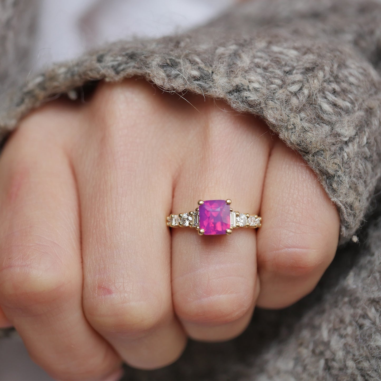 This exquisite ring showcases a rare unheated cushion cut opalescent ruby-colored sapphire, surrounded by eight dazzling diamonds in round, carré, and baguette cuts, offering a perfect blend of vibrant color and sparkling brilliance in a luxurious design.