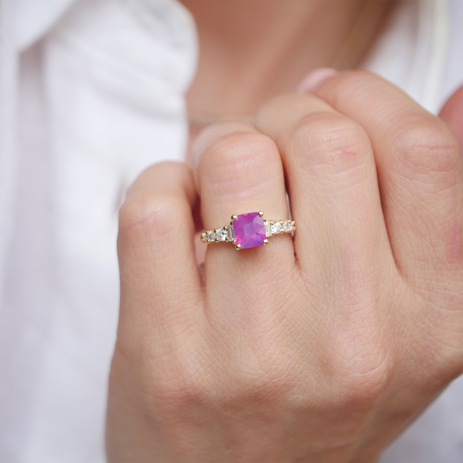 A captivating unheated cushion cut opalescent ruby-colored sapphire is the centerpiece of this ring, encircled by eight diamonds in various cuts—round, carré, and baguette—creating a dazzling contrast of color and light.