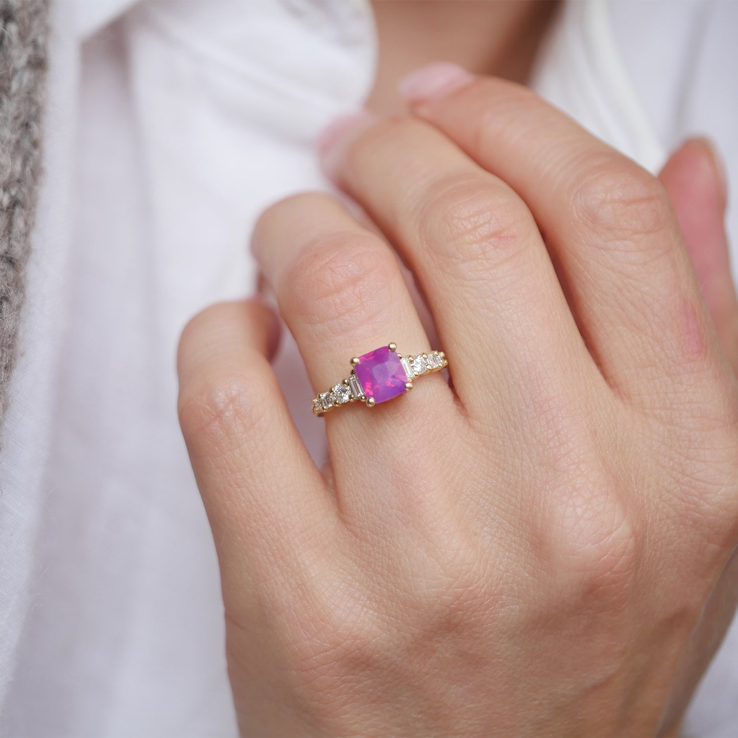 Set in a timeless design, this unheated cushion cut opalescent ruby-colored sapphire is surrounded by eight natural round, carré, and baguette diamonds, creating a luxurious halo that enhances the sapphire’s rich hue and brilliance.