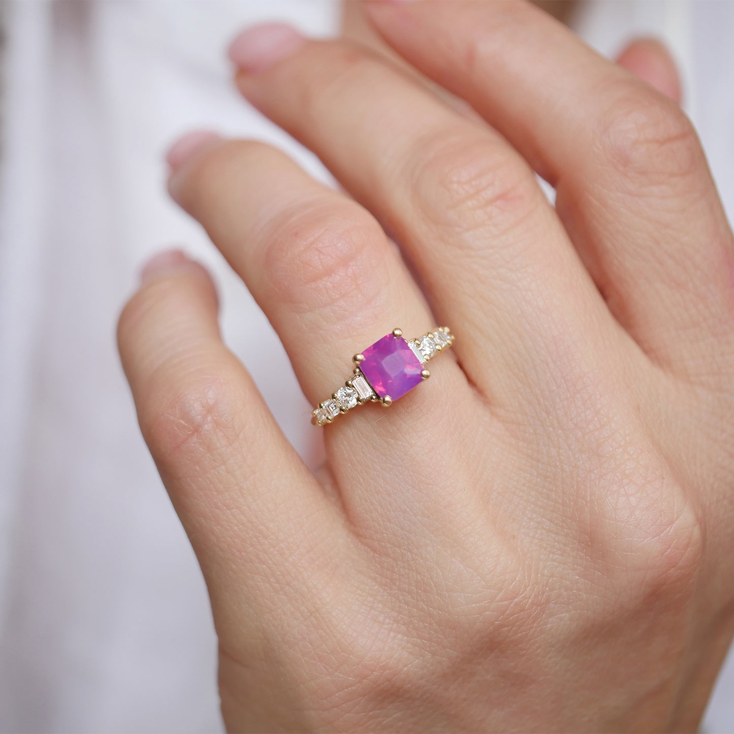 Featuring a gorgeous unheated cushion cut opalescent ruby-colored sapphire, this ring is accentuated by eight diamonds—round, carré, and baguette cuts—adding a brilliant touch to the sapphire’s opalescent glow for a sophisticated and luxurious piece.