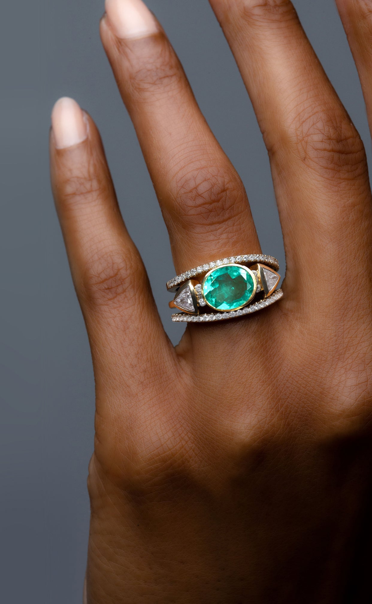 Woman wearing a yellow gold diamond and emerald gemstone engagement ring and wedding bands