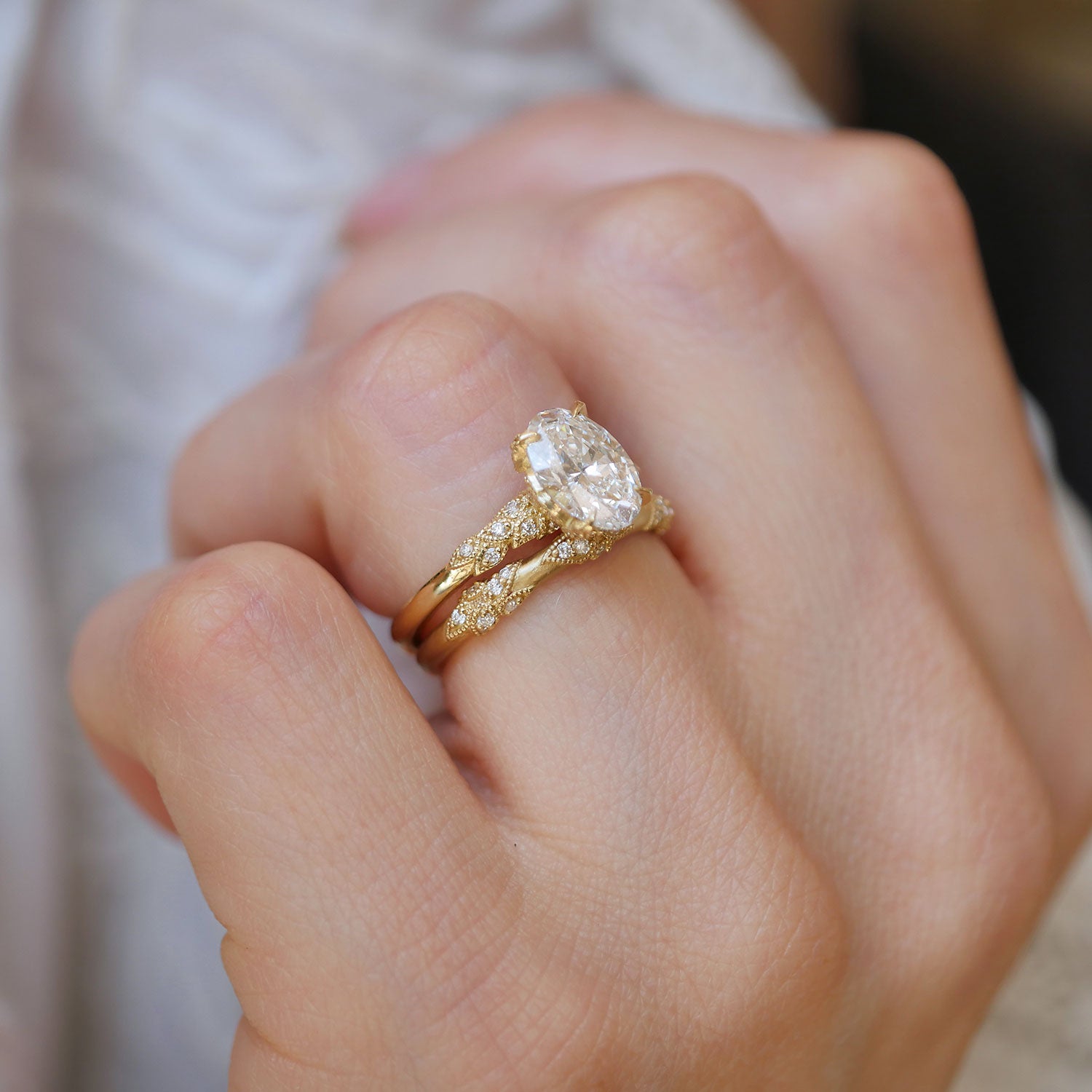 Close-up of a hand wearing two nature-inspired gold rings with diamond accents.