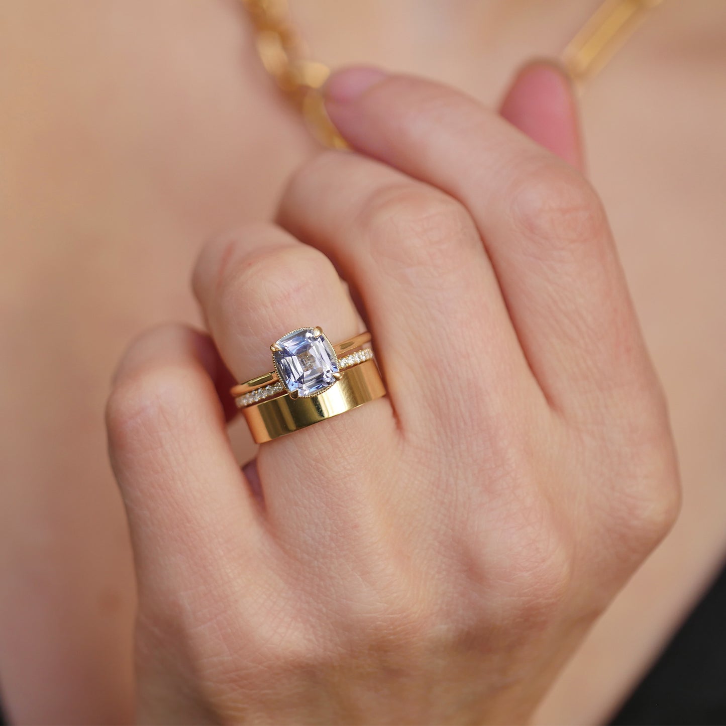 woman wearing cornflower blue sapphire solitaire engagement ring with diamond and gold stacking bands