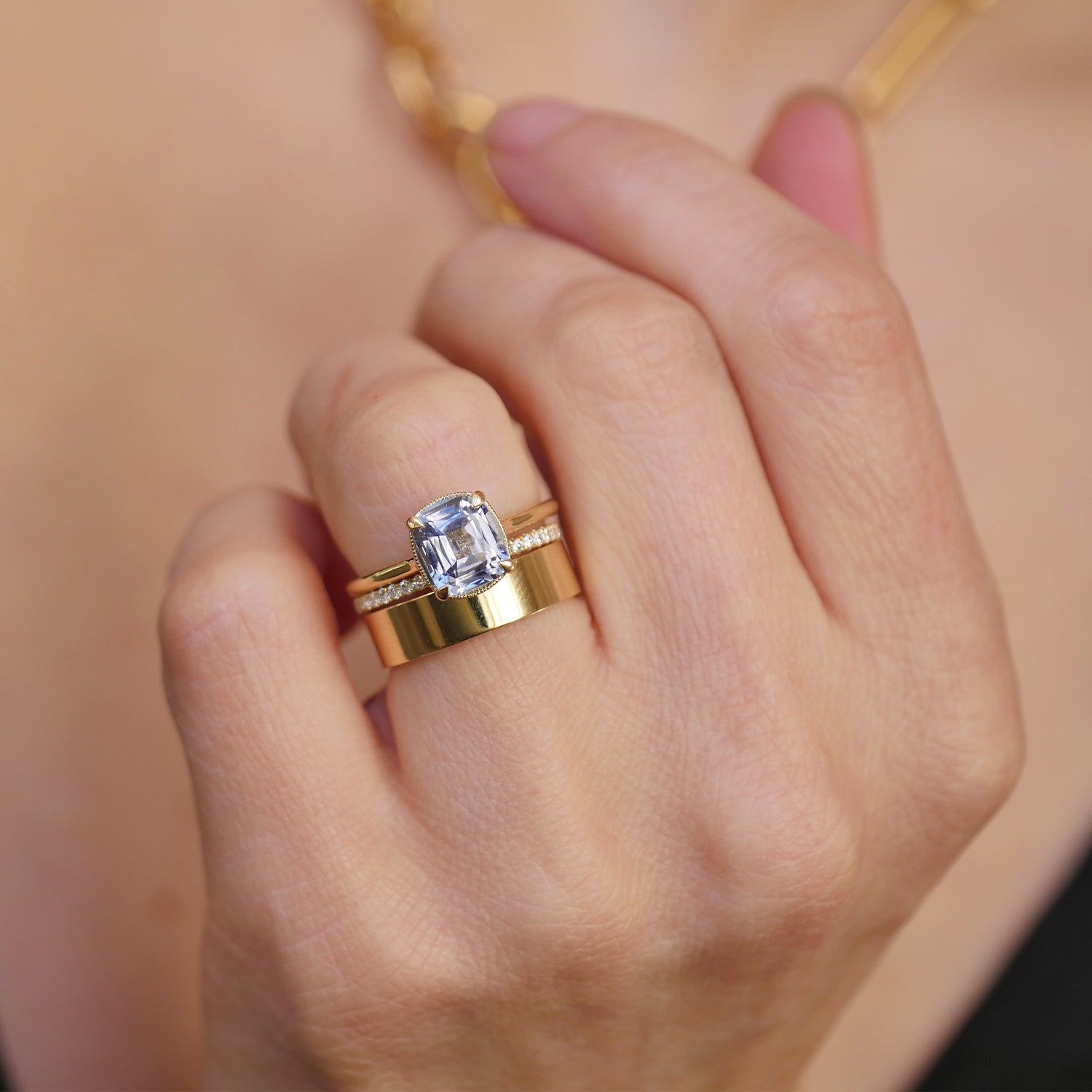 woman wearing cornflower blue sapphire solitaire engagement ring with diamond and gold stacking bands