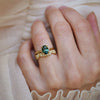 Close-up of a hand wearing a nature inspired gold band with a green sapphire engagement ring.
