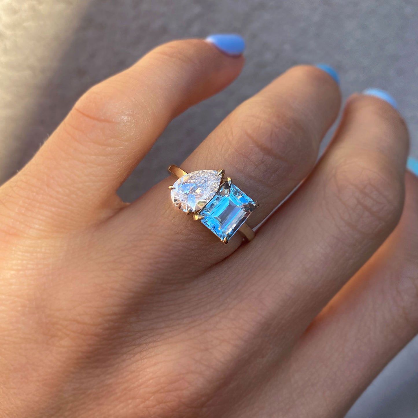 The Aquamarine & Pear Diamond Toi et Moi Ring features a stunning combination of a soft blue aquamarine gemstone and a sparkling pear-shaped diamond, creating an elegant and harmonious design.